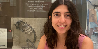 A photo of Iris in front of a showcase displaying a fossil of a rodant.