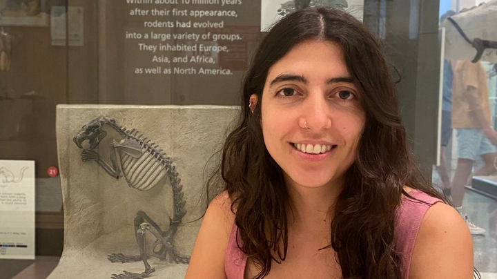 A photo of Iris in front of a showcase displaying a fossil of a rodant.