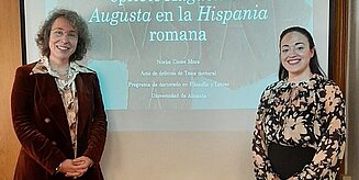 Henriette Herz-Scout Sabine Panzram und Humboldt-Stipendiatin Noelia Cases Mora stehen gemeinsam vor einer Vortrags-Projektion